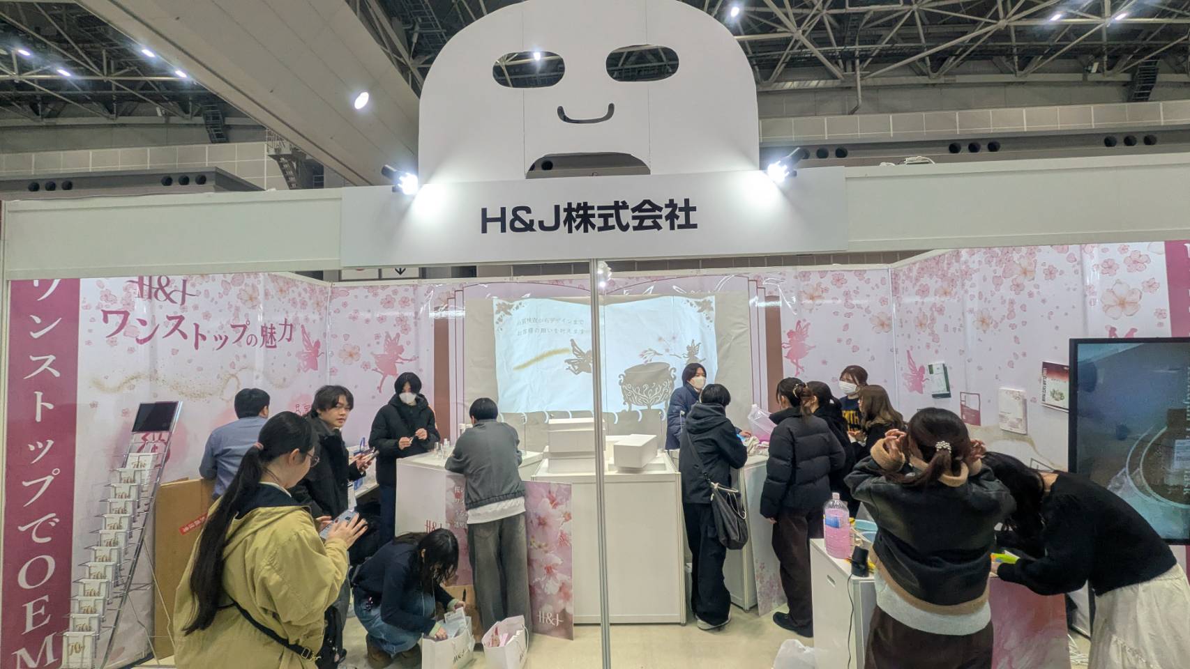 大型フェイスマスクモデルと来場者で賑わうH&J株式会社のブース全景
